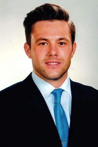 Roberto Ugarte — formal headshot in a dark suit and teal tie against a light background.