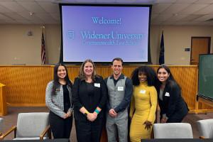 Five people stand together in front of a Widener University Commonwealth Law School welcome screen in what appears to be a classroom or moot courtroom, smiling for a group photo at a Center for Equity and Justice Student Fellows event.