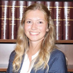 Megan Bisco smiles in a portrait in front of shelves of law books, wearing a navy blazer.