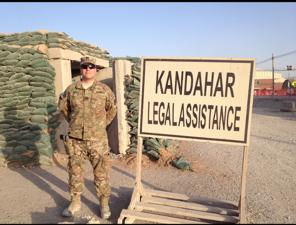WLC alumnus Stephen Romeo in military fatigues next to a sign that reads KANDAHAR LEGAL ASSISTANCE