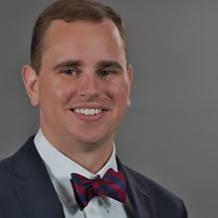 Matthew V. Kerns — smiling headshot in a navy suit and burgundy bow tie, against a gray studio background.