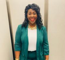 Arlene Marshall-Hockensmith — Smiling woman in a teal blazer with a gold statement necklace, photographed indoors.