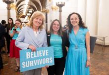Photo of alumnus standing with colleagues, one holding a sign that says "believe survivors"