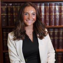 Kiera Flannery — smiling headshot in a white blazer, posed in front of law library shelves.