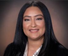 Kimberly Diaz smiles in a professional headshot wearing a dark blazer against a warm brown studio background.