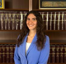 Haley Nelson smiles in a portrait wearing a blue blazer, seated in front of shelves of law books.