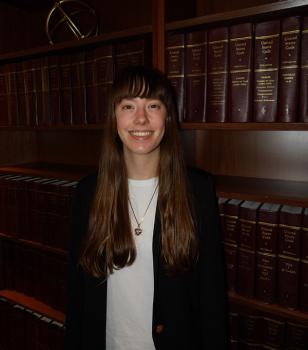 Brianna Bitler smiles in a portrait in front of shelves of United States Code volumes, wearing a black blazer over a white top.
