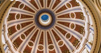 Looking straight up into the ornate interior of the Pennsylvania State Capitol dome, featuring intricate gold, red, and blue decorative details radiating from a central skylight.
