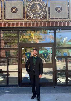 WLC student Hunter in a suit standing in front of a building with signs that read OCEAN COUNTY NEW JERSEY and OFFICE OF THE COUNTY PROSECUTOR.