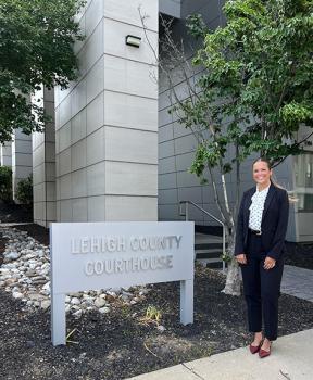 Law student Riley in a suit standing next to a sign that reads LEHIGH COUNTY COURTHOUSE.
