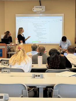 student gesturing to the screen at the front of the classroom