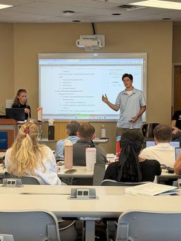 student gesturing to the screen at the front of the classroom