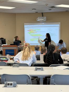 student gesturing to the screen at the front of the classroom