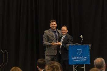 Dean andre douglas pond cummings on stage posing with Daniel Schramm '17 with an award. 